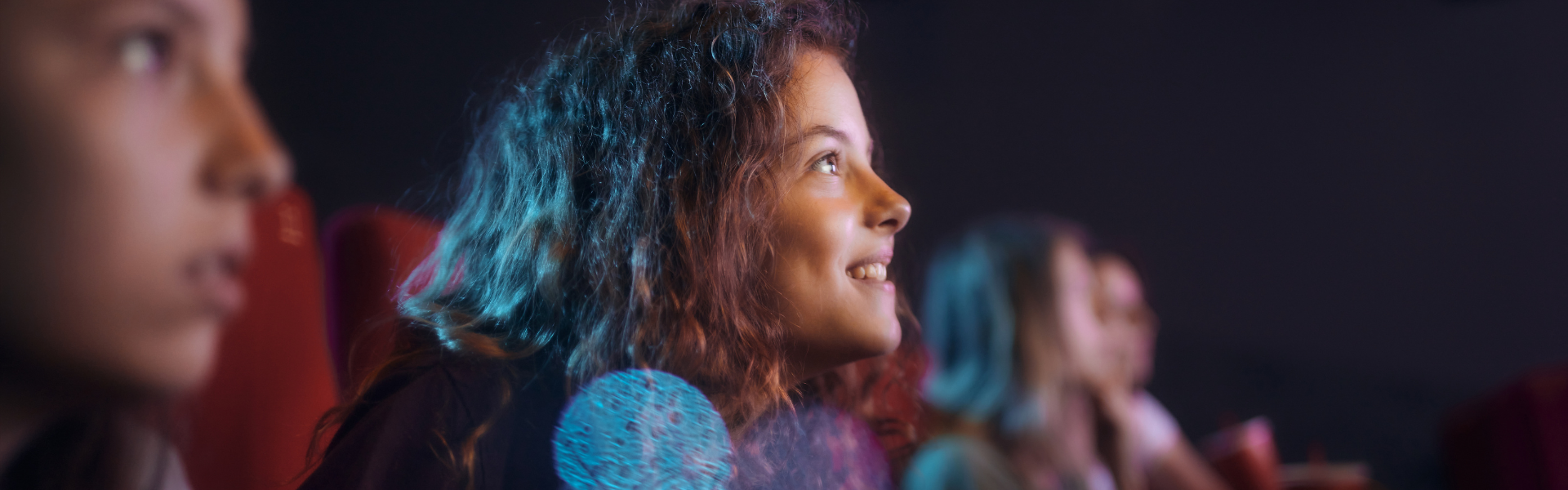 Young girl with curly hair sitting in theatre seats looking at stage in awe