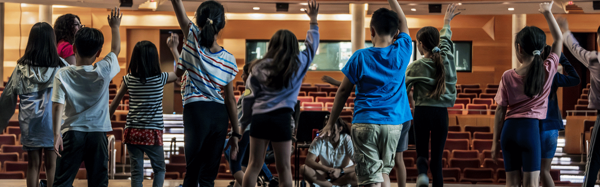 A row of youth rehearsing a theatre number on a stage in front of auditorium seats