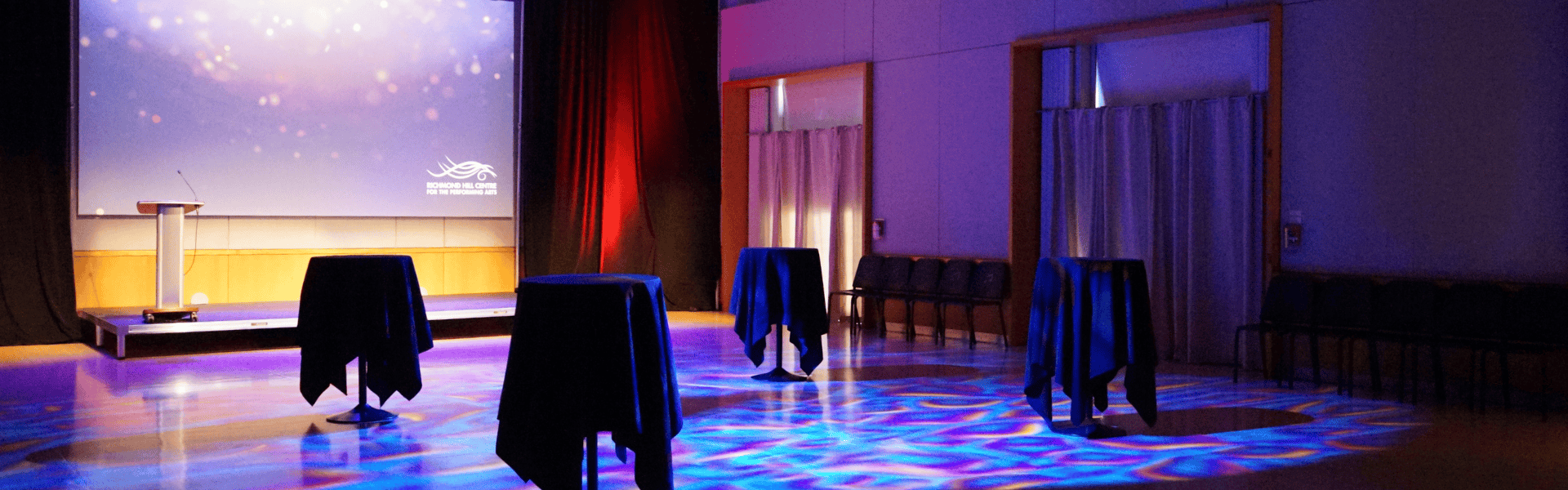 Swirling multi-colour floodlight illuminates hall floor, surrounded by cruiser tables and a small stage